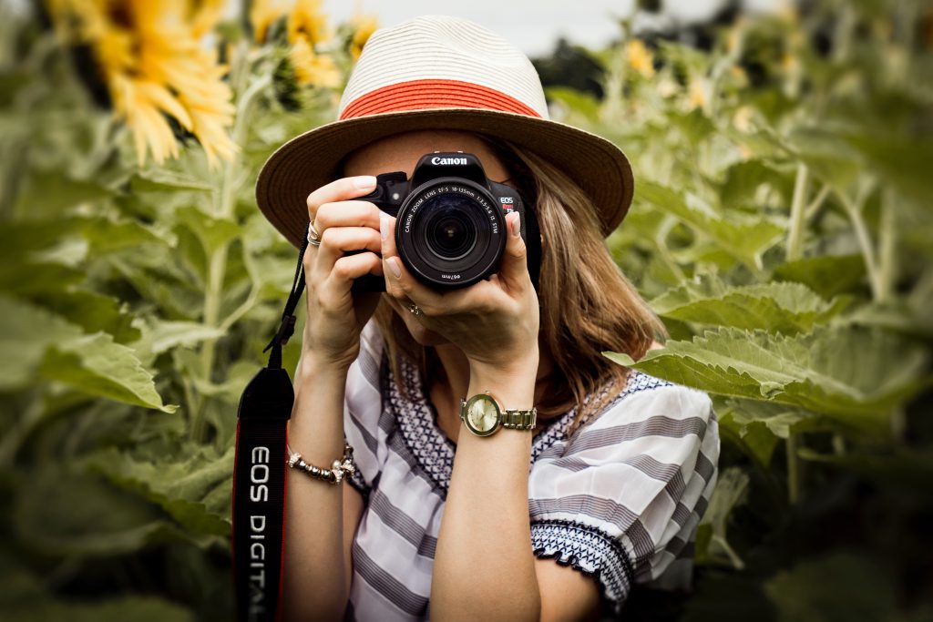 Woman taking a photo in a field of sunflowers, pointing her camera at us